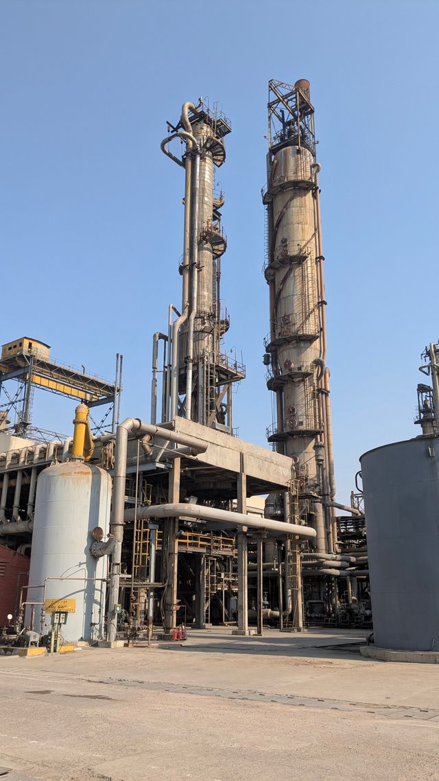 View of industrial refinery towers in a factory setting under clear blue skies, showcasing industrial architecture.