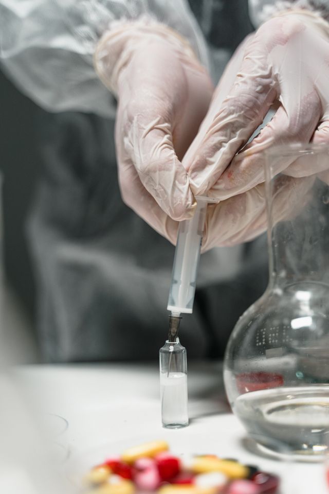 Scientist uses syringe to inject liquid into vial, showcasing laboratory work.